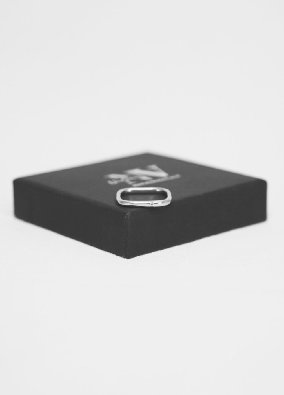 טבעת לילי עדינה מרובעת ועם אבן קטנה בצד במקום באמצע מונחת על קופסה שחורה עם לוגו נינה ולרו