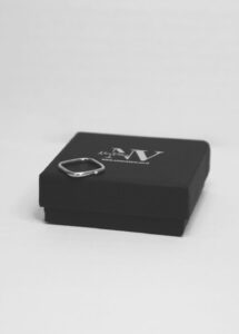 טבעת לילי עדינה מרובעת ועם אבן קטנה בצד במקום באמצע מונחת על קופסה שחורה עם לוגו נינה ולרו