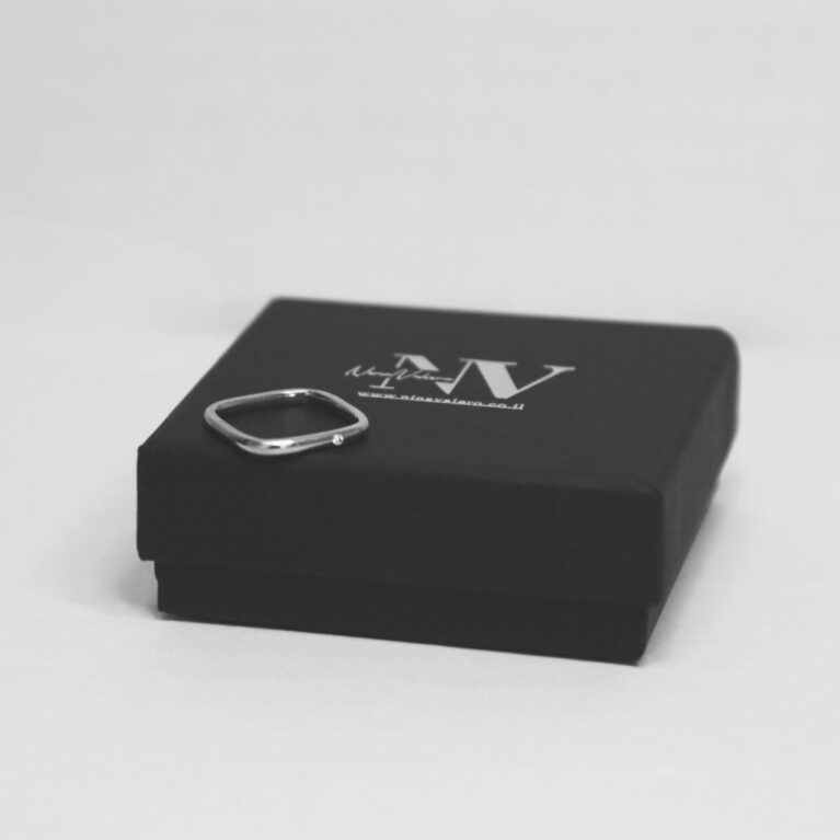 טבעת לילי עדינה מרובעת ועם אבן קטנה בצד במקום באמצע מונחת על קופסה שחורה עם לוגו נינה ולרו