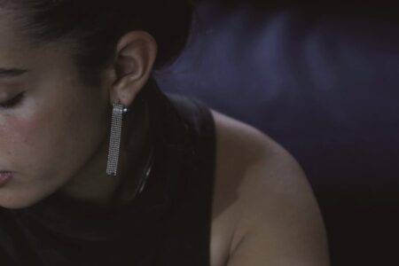 דוגמנית בחצי פרופיל עונדת את עגיל לורן - חישוק קטן ועבה שמוצמדים לו שרשראות כדורים קטנות נשפכות ממנו