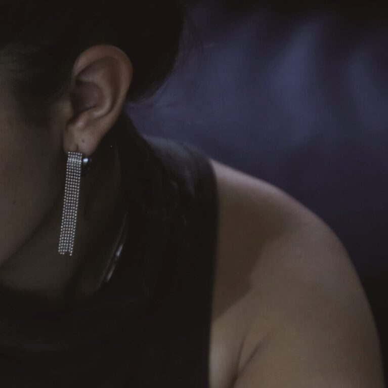 דוגמנית בחצי פרופיל עונדת את עגיל לורן - חישוק קטן ועבה שמוצמדים לו שרשראות כדורים קטנות נשפכות ממנו